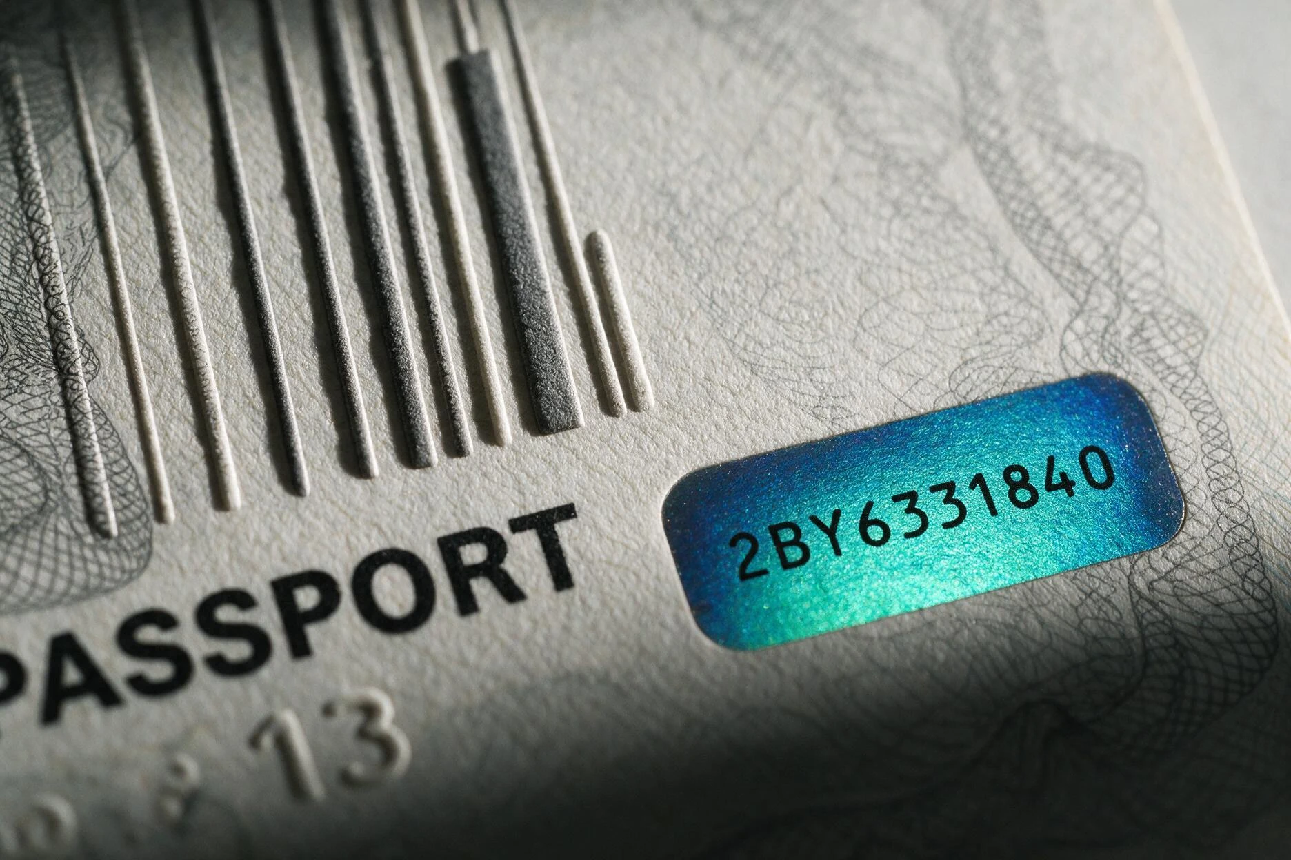 A passport data page under raking light, showing raised intaglio print and a colour-shifting security element